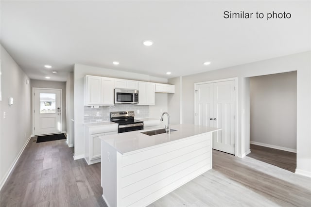 kitchen with backsplash, stainless steel appliances, a kitchen island with sink, sink, and white cabinets