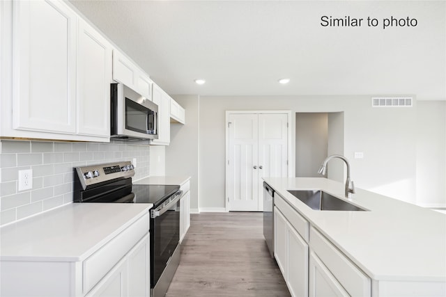 kitchen with white cabinetry, sink, light hardwood / wood-style floors, a kitchen island with sink, and appliances with stainless steel finishes