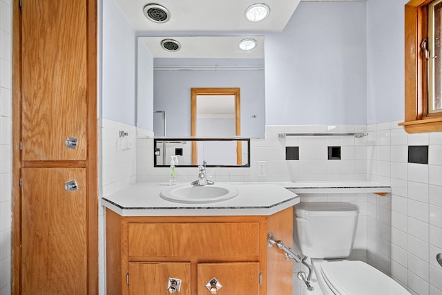 bathroom with vanity, toilet, and tile walls