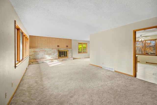 unfurnished living room featuring a textured ceiling, light colored carpet, ceiling fan, wooden walls, and a fireplace