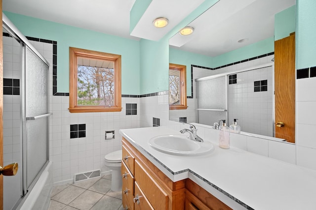 full bathroom with vanity, shower / bath combination with glass door, tile patterned floors, toilet, and tile walls