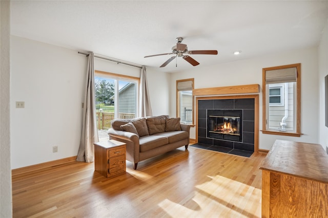 living room featuring ceiling fan, light wood-type flooring, and a tiled fireplace