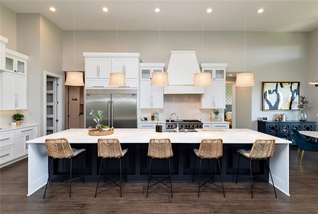 kitchen featuring a kitchen bar, backsplash, a large island, white cabinets, and built in fridge