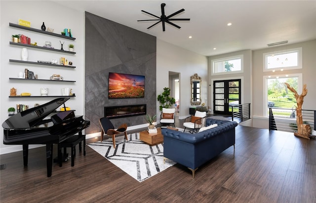 living room with ceiling fan, french doors, a high end fireplace, dark hardwood / wood-style floors, and a towering ceiling