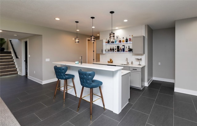 bar with gray cabinetry, decorative light fixtures, backsplash, and sink