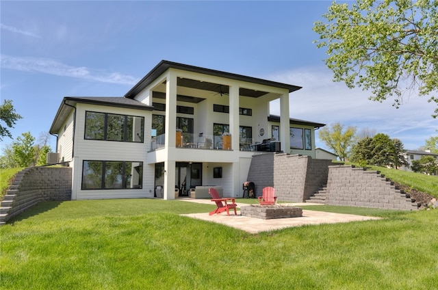 rear view of property featuring a balcony, ceiling fan, an outdoor fire pit, a patio, and a lawn