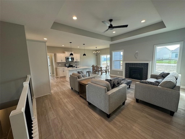 living room with a tray ceiling, sink, and light wood-type flooring