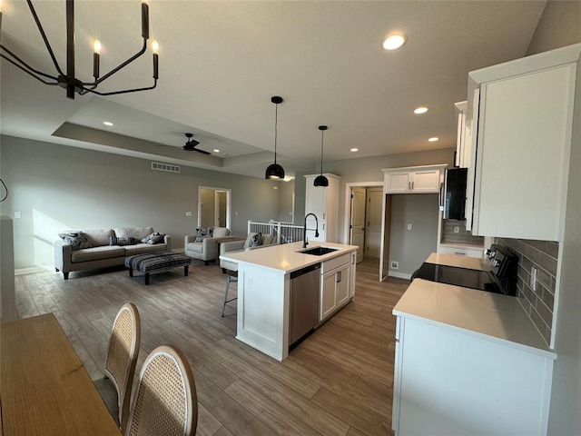 kitchen with stainless steel dishwasher, black range oven, sink, white cabinets, and an island with sink