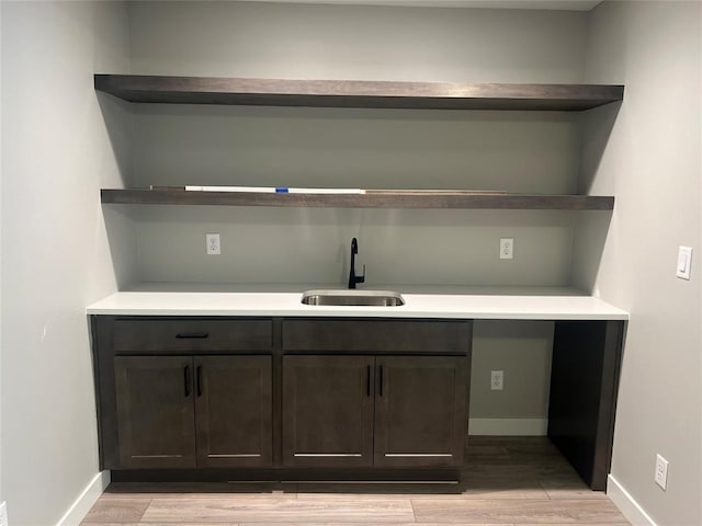 bar with dark brown cabinets, light hardwood / wood-style floors, and sink