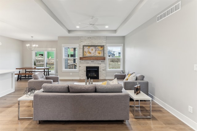 living room with a brick fireplace, ceiling fan with notable chandelier, light hardwood / wood-style flooring, and a raised ceiling