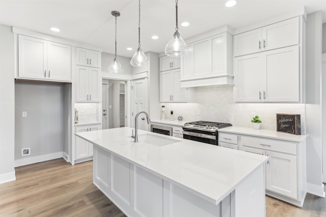 kitchen with sink, stainless steel gas range oven, pendant lighting, a center island with sink, and white cabinets