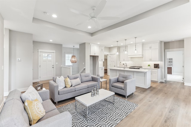 living room featuring light wood-type flooring, a tray ceiling, and ceiling fan