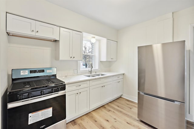 kitchen featuring sink, stainless steel refrigerator, white cabinetry, black gas stove, and light stone counters