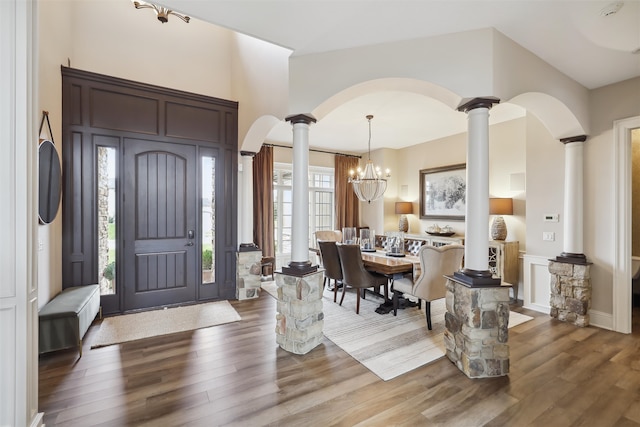 foyer entrance with a chandelier, ornate columns, and dark wood-type flooring