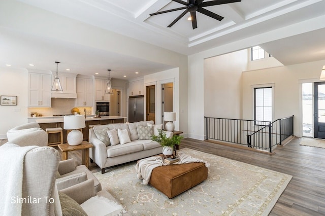 living room with light wood-type flooring, coffered ceiling, ceiling fan, sink, and beam ceiling