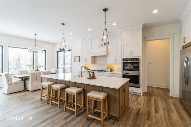 kitchen featuring white cabinets, an island with sink, decorative light fixtures, and appliances with stainless steel finishes