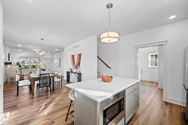 kitchen with stainless steel microwave, light wood-type flooring, decorative light fixtures, a kitchen island, and a breakfast bar area