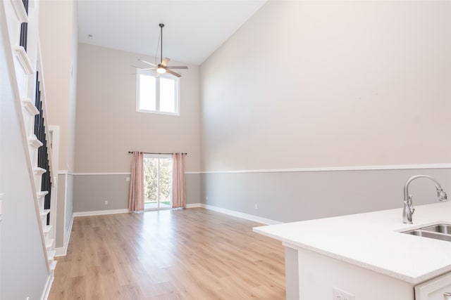 unfurnished living room with ceiling fan, sink, high vaulted ceiling, and light hardwood / wood-style flooring