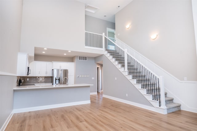 kitchen featuring white cabinetry, a high ceiling, light hardwood / wood-style flooring, kitchen peninsula, and appliances with stainless steel finishes