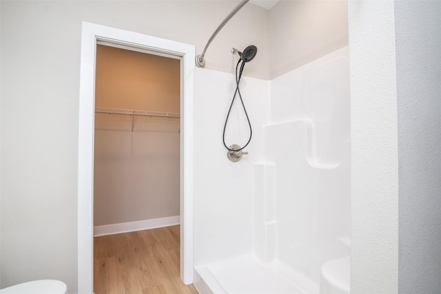 full bath featuring a walk in closet, a shower stall, toilet, and wood finished floors