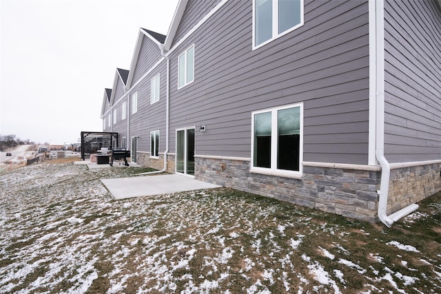 snow covered rear of property featuring a patio