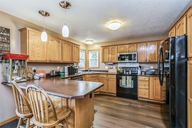 kitchen with dark wood-type flooring, kitchen peninsula, pendant lighting, a textured ceiling, and black appliances