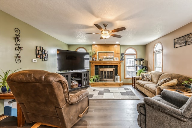 living room featuring a tile fireplace, a textured ceiling, hardwood / wood-style flooring, and ceiling fan