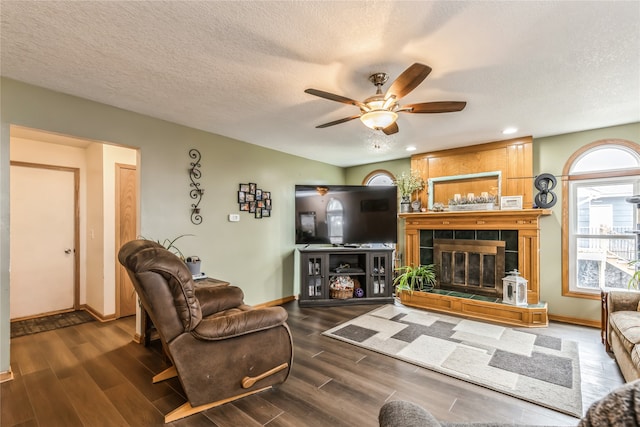 living room with a tiled fireplace, ceiling fan, dark wood-type flooring, and a textured ceiling