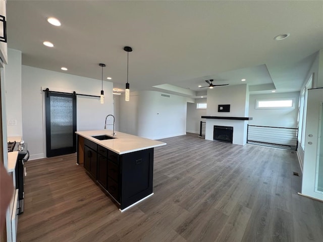 kitchen featuring dark hardwood / wood-style flooring, sink, a barn door, decorative light fixtures, and an island with sink