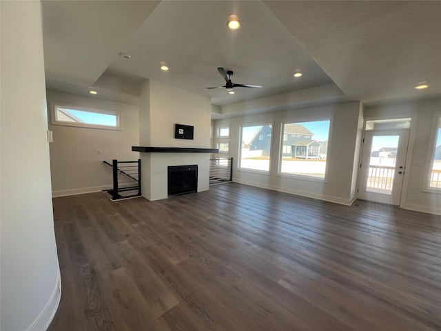 unfurnished living room with ceiling fan, dark wood-type flooring, and a tray ceiling