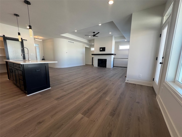 kitchen with pendant lighting, dark hardwood / wood-style flooring, sink, a kitchen island with sink, and ceiling fan