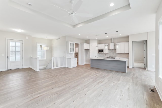 unfurnished living room featuring ceiling fan with notable chandelier, light hardwood / wood-style floors, sink, and a tray ceiling