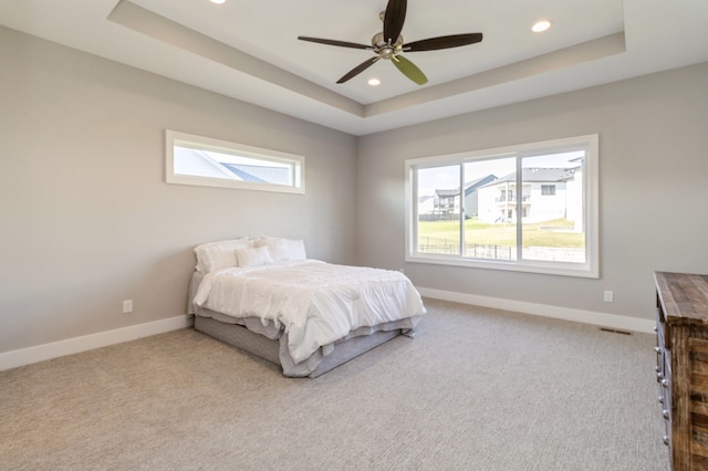 bedroom with light carpet, a raised ceiling, multiple windows, and ceiling fan