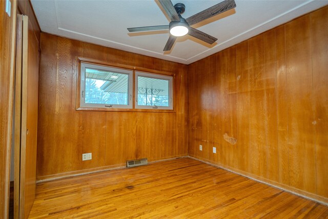 spare room featuring wooden walls, ceiling fan, and light hardwood / wood-style floors