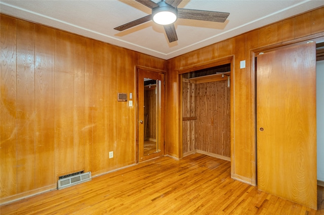 unfurnished bedroom featuring a closet, light hardwood / wood-style floors, ceiling fan, and wooden walls