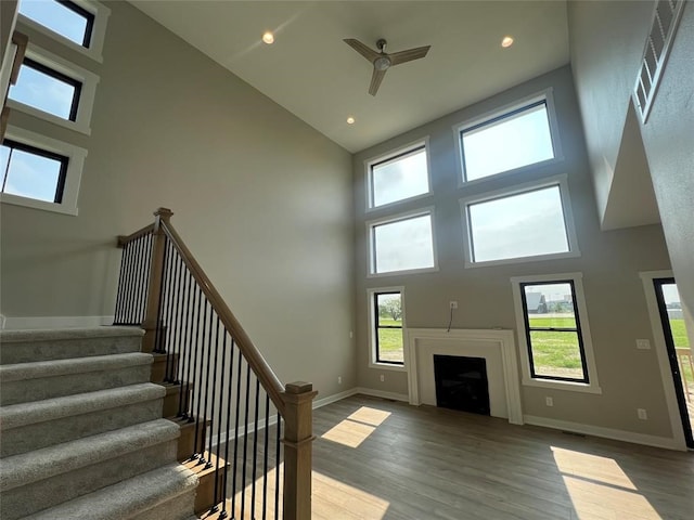 unfurnished living room featuring a high ceiling, ceiling fan, and hardwood / wood-style floors