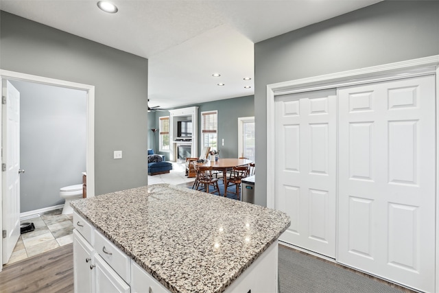 kitchen with ceiling fan, dark wood-type flooring, a kitchen island, light stone counters, and white cabinets