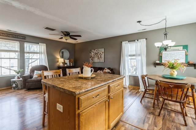 kitchen with a kitchen bar, ceiling fan with notable chandelier, decorative light fixtures, hardwood / wood-style flooring, and a center island