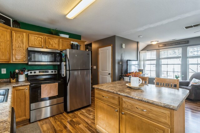 kitchen with appliances with stainless steel finishes, a textured ceiling, dark hardwood / wood-style floors, and a kitchen island