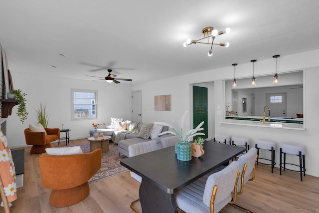 living room with sink, ceiling fan with notable chandelier, and light wood-type flooring