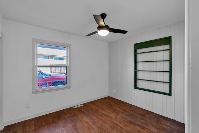 spare room with ceiling fan, wooden walls, and dark wood-type flooring