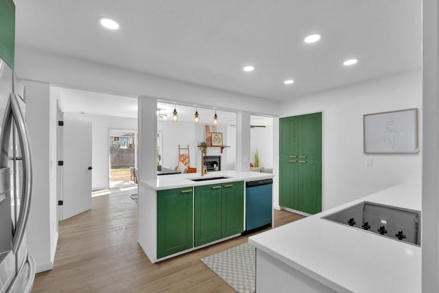 kitchen with a large fireplace, stainless steel appliances, light hardwood / wood-style flooring, and green cabinets