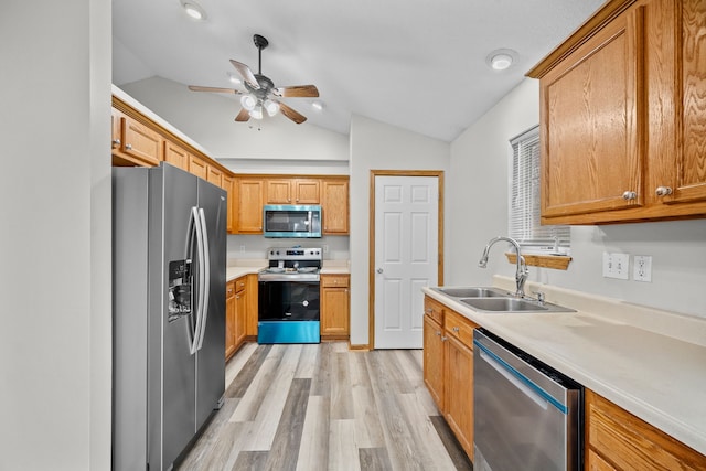 kitchen with stainless steel appliances, a sink, light wood-style floors, vaulted ceiling, and light countertops