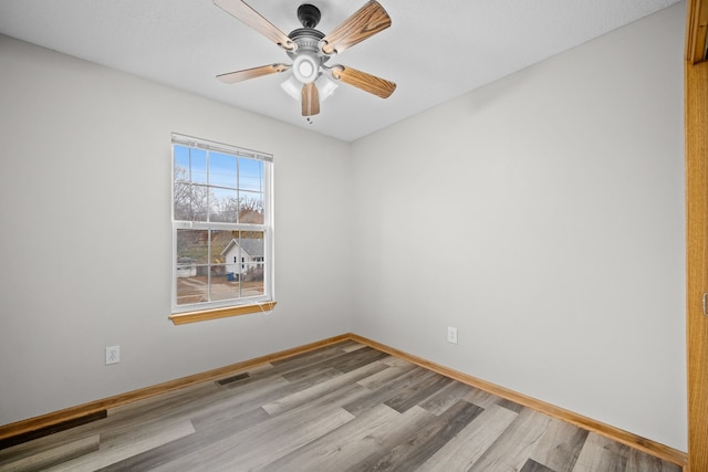 empty room with a ceiling fan, visible vents, baseboards, and wood finished floors