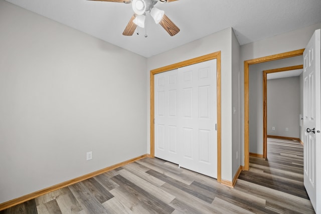 unfurnished bedroom featuring a closet, ceiling fan, baseboards, and wood finished floors