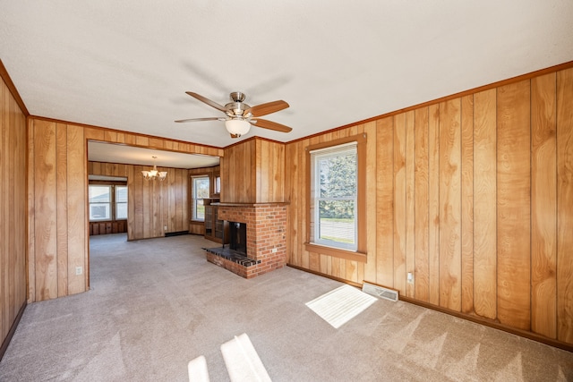 unfurnished living room with light carpet, ornamental molding, ceiling fan with notable chandelier, wooden walls, and a fireplace