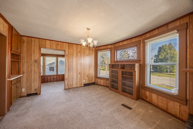 interior space with a textured ceiling, wooden walls, light colored carpet, and a notable chandelier