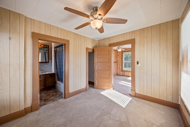 unfurnished bedroom featuring ceiling fan, wood walls, carpet floors, and ensuite bathroom