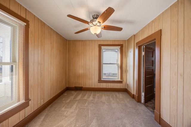 carpeted empty room with wood walls, ceiling fan, and a healthy amount of sunlight