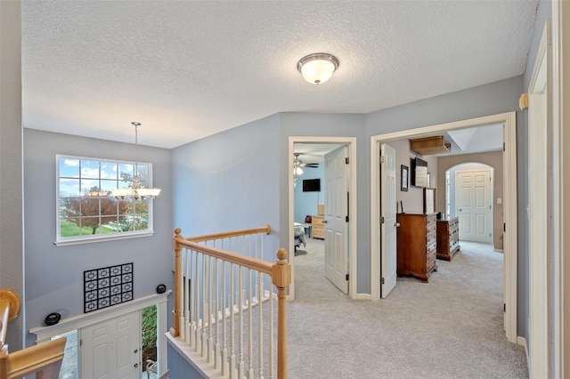 corridor featuring a textured ceiling, light colored carpet, and a chandelier